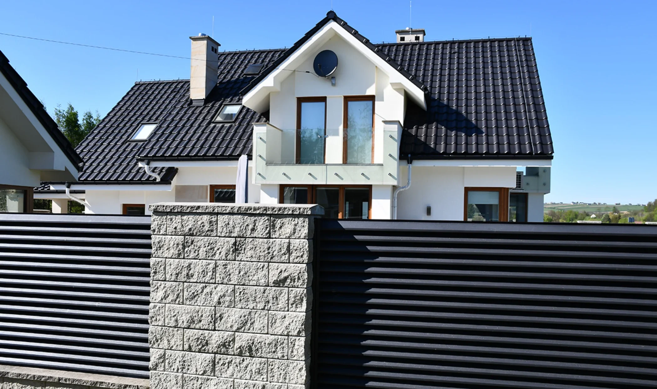 Moderner Lamellenzaun aus Aluminium auf Betonsockel vor weißem Einfamilienhaus mit Balkon