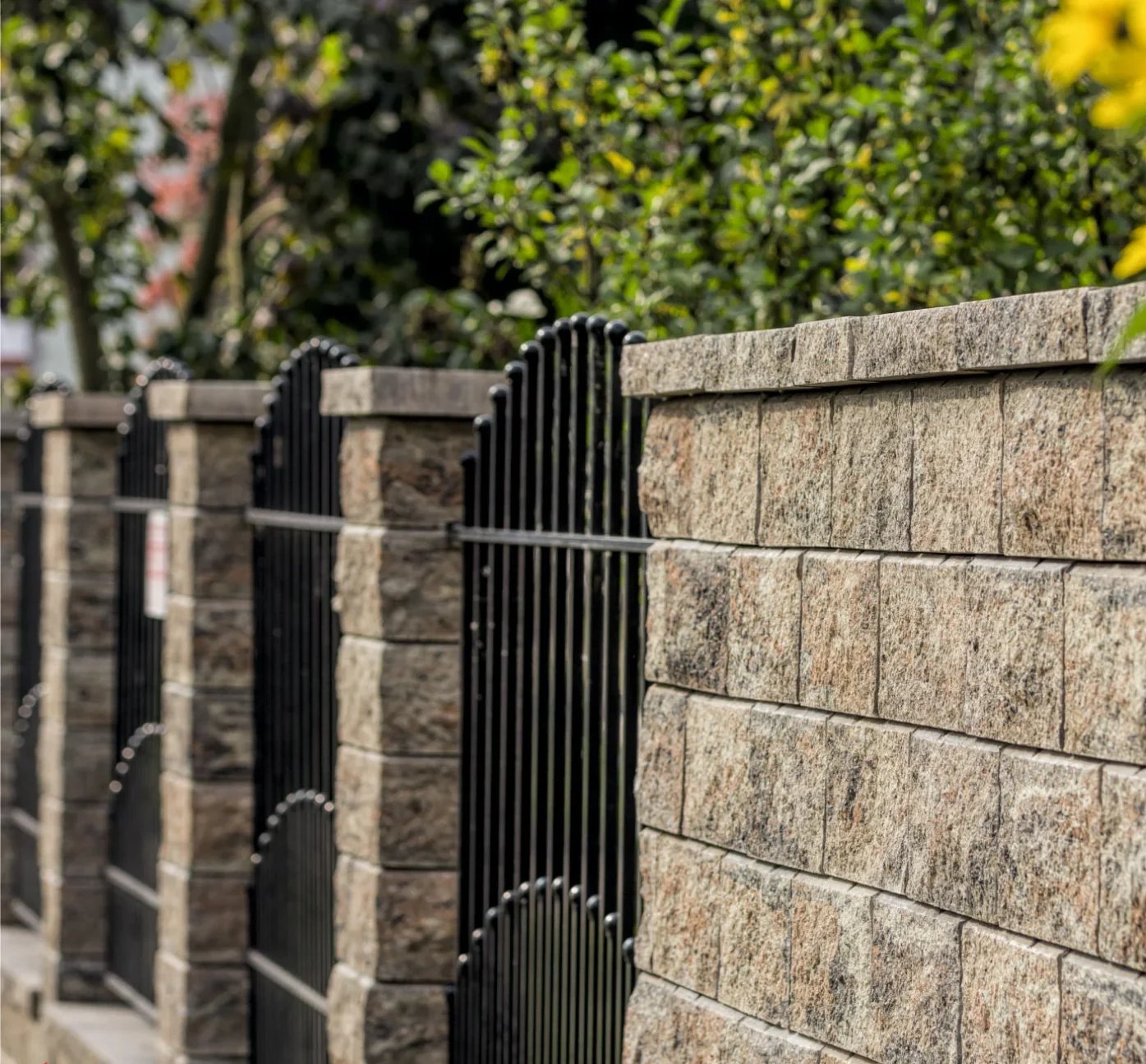 Betonzaun mit schwarzem Metallgeländer vor begrüntem Hintergrund