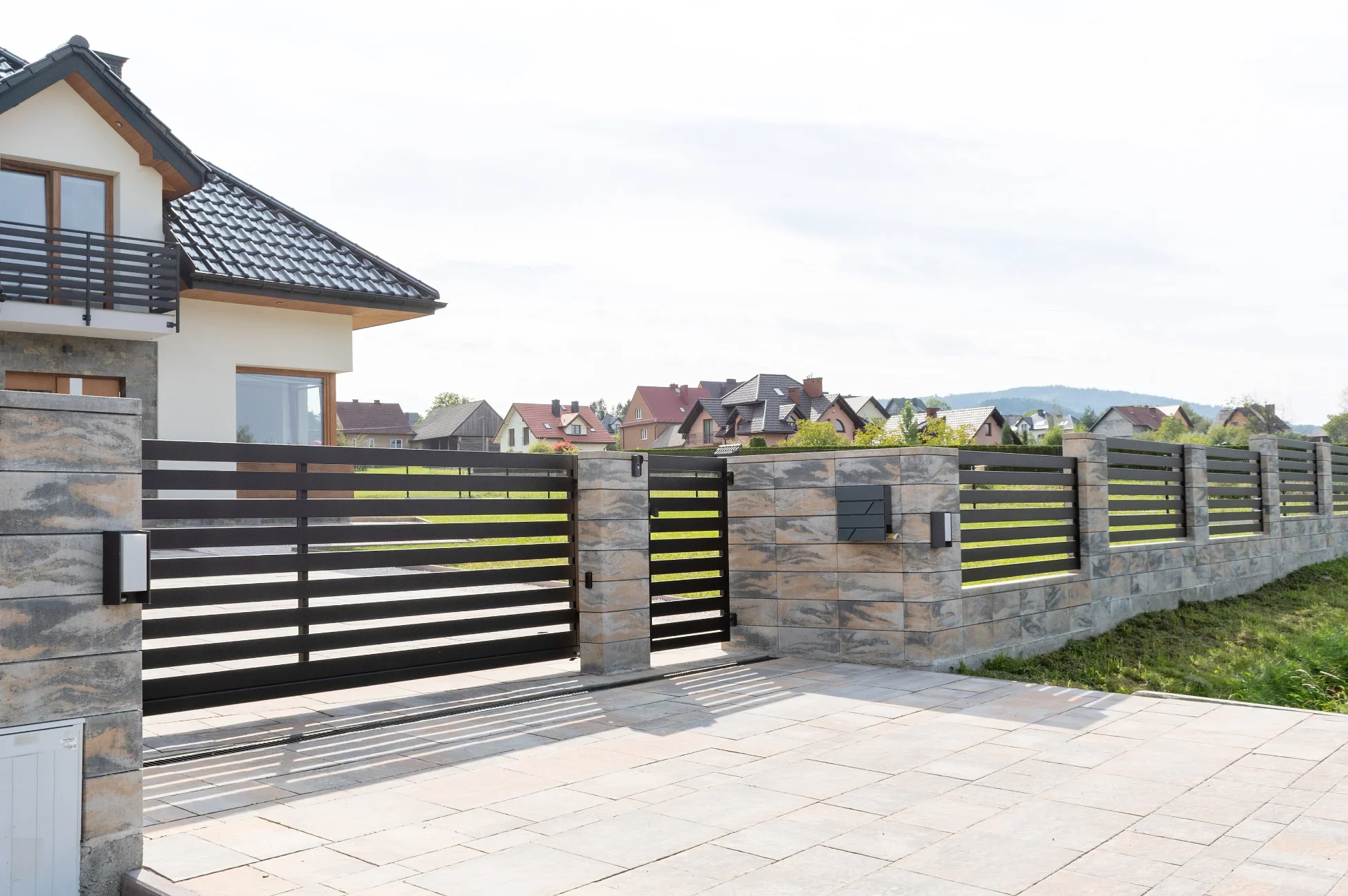 Moderner Lamellenzaun aus Metall mit Natursteinpfeilern vor Einfamilienhaus