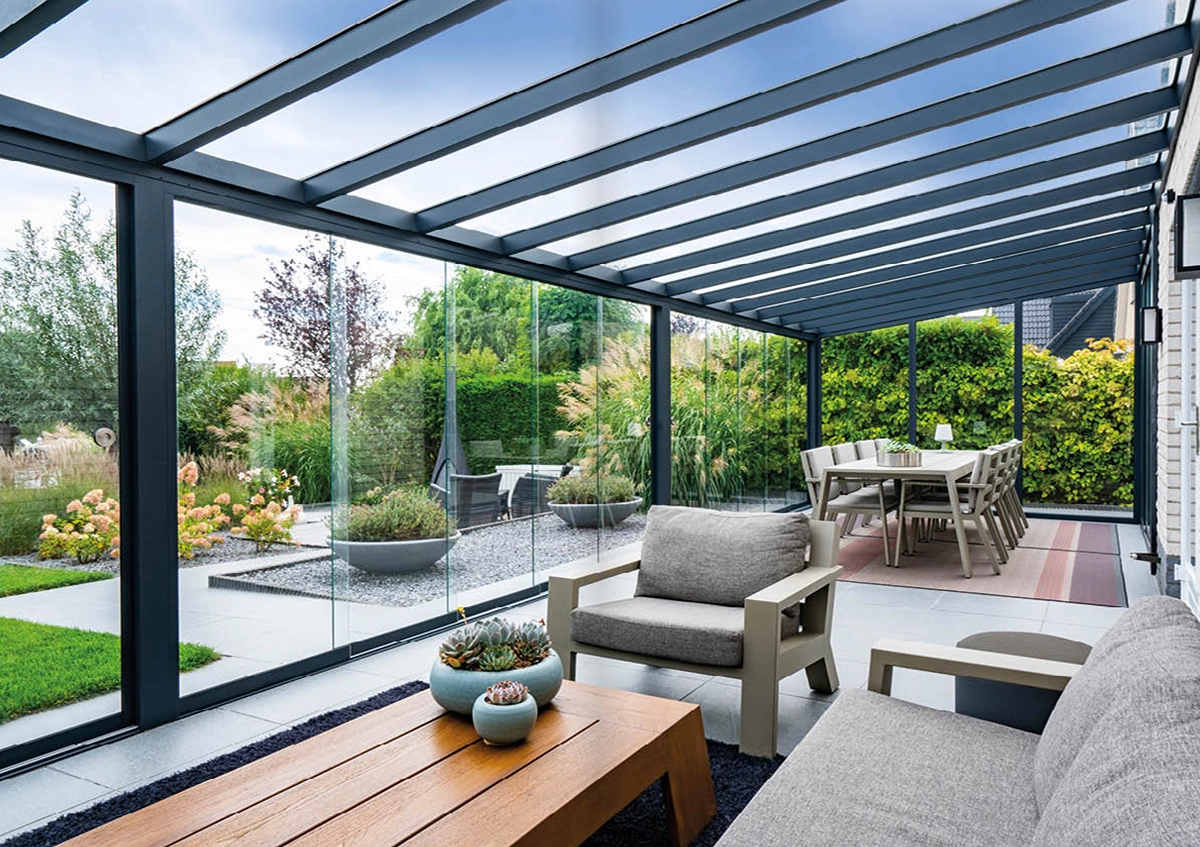 Moderner Wintergarten mit Glasdach und Loungemöbeln neben gepflegtem Garten